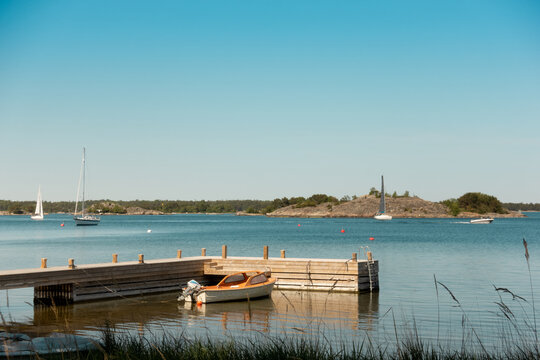 Stockholm Archipelago In Sunset With Small Boat Moored To Pier With Sailing Boats Anchored In Background