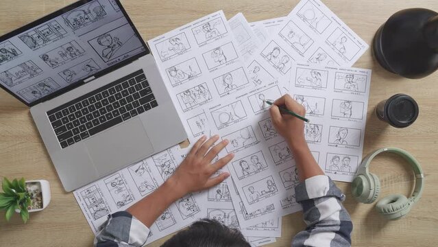 Close Up Top View Of Asian Male Artist Drawing Storyboard For The Film On The Table With A Laptop And Headphones In The Studio
