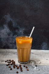 Ice coffee in a tall glass. Cold summer drink on a dark wooden background with copy space. 