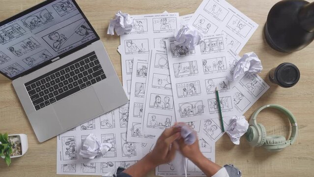 Close Up Top View Of Male Artist'S Hands Crumples Paper Before Throwing While Drawing Storyboard For The Film On The Table With A Laptop And Headphones In The Studio
