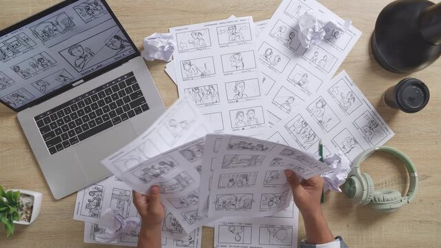 Close Up Top View Of Male Artist'S Hands Holding Sketching Papers, Choosing, Then Throwing On The Table With A Laptop And Headphones In The Studio
