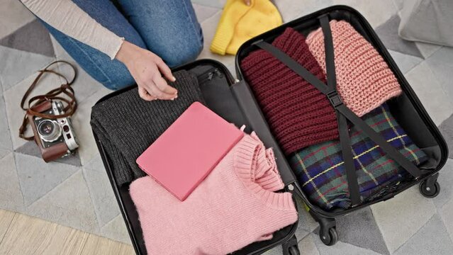 Young blonde woman packing clothes on suitcase for journey at home