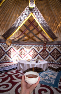 a cup of tea in a man's hand behind a dastarkhan in the Kazakh national yurt