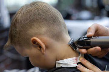 The barber's hand shaves the hair on the back of the child's head in a beauty salon The child is...