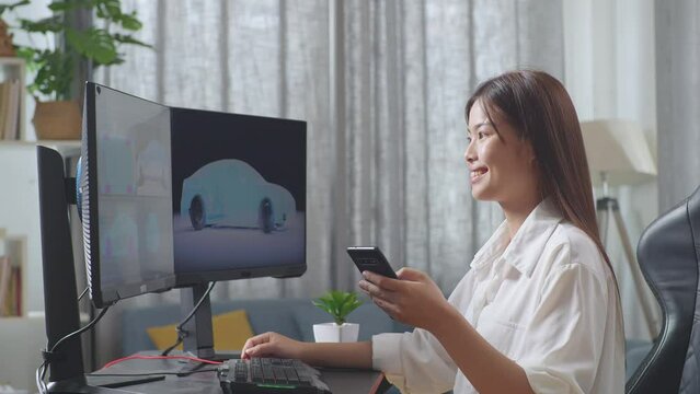 Side View Of Asian Female Automotive Designer Comparing The 3D Model Of Ev Car On The Desktop Computers To The Photo On Her Smartphone In The Studio
