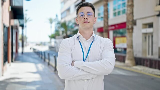 Young hispanic man standing with serious expression and arms crossed gesture at street