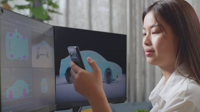 Close Up Side View Of Asian Female Automotive Designer Comparing The 3D Model Of Ev Car On The Desktop Computers To The Photo On Her Smartphone In The Studio
