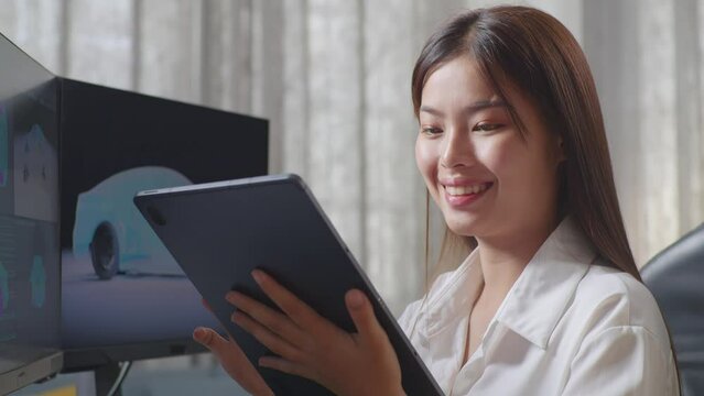 Close Up Side View Of Asian Female Automotive Designer Comparing The 3D Model Of Ev Car On The Desktop Computers To The Photo On Her Tablet In The Studio
