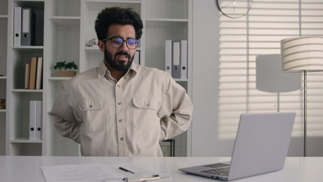 Tired exhausted Indian muslim man businessman unwell male office entrepreneur feel back muscle tension backache pain after laptop business work massaging spine spasm relief sick guy has health problem
