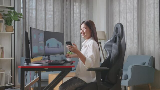 Side View Of Asian Female Automotive Designer Looking At Her Smartphone Then Celebrating The Success While Working On 3D Model Of Ev Car On The Desktop Computers In The Studio
