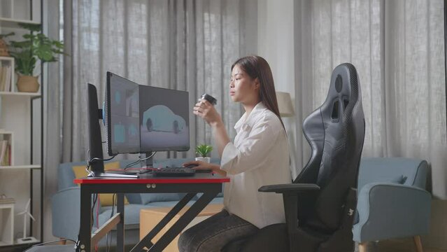 Side View Of Asian Female Automotive Designer Drinking Coffee While Working On 3D Model Of Ev Car On The Desktop Computers In The Studio
