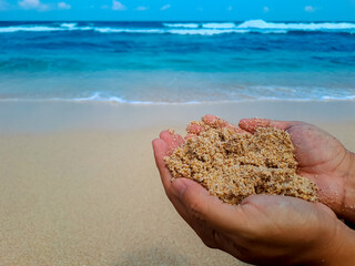 Human hand holding sand with view of beach in the background. Summer holiday concept