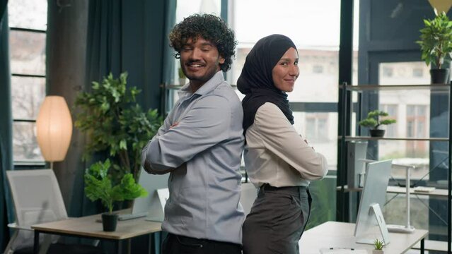Two happy business partners diverse multiracial colleagues managers entrepreneurs Muslim businesswoman in hijab and Arabian latino businessman in corporate office posing crossed hands team partnership