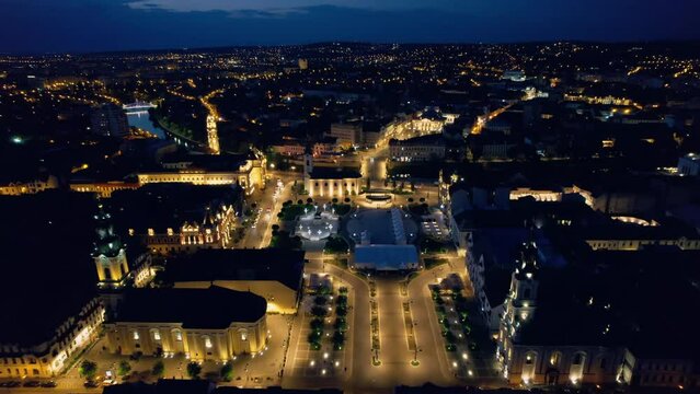 Areal drone view of the Unirii Square in Oradea downtown at night, Romania. Moon Church, Cathedral of St. Nicholas and other historical buildings, illumination