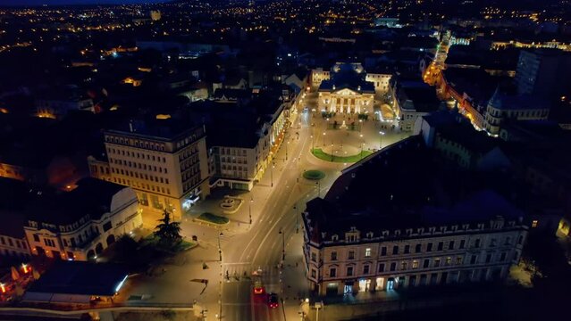 Aerial drone view of Oradea downtown at night, Romania. Crisul Repede river, State Theatre with people coming out, illumination