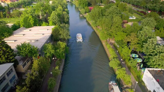 Aerial drone view of Bega river in Timisoara, Romania. View of the river with floating boat, greenery on the both sides of the river and buildings in the distance