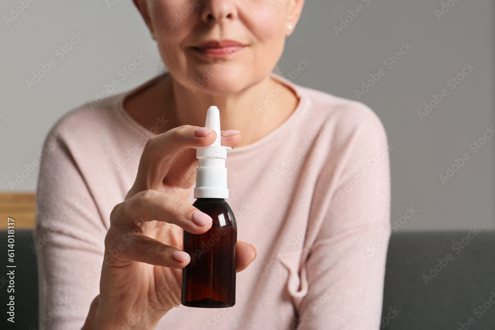 Poster Woman holding nasal spray indoors, focus on bottle