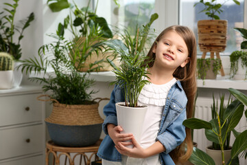 Cute little girl holding beautiful green plant at home. House decor