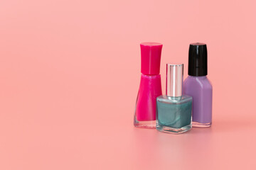 Pink, purple and teal nail polish bottles on pink background. Copy space.