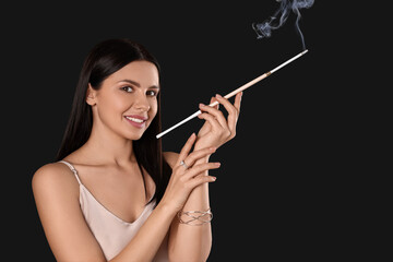 Woman using long cigarette holder for smoking on black background, space for text