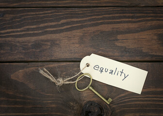 The key of equality concept isolate. Gold key with a label on wood table. Equal status or level.