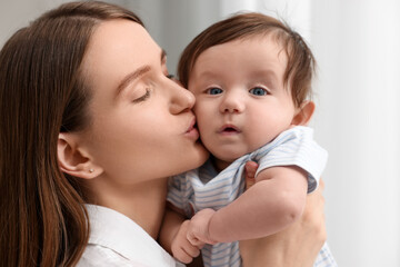 Happy mother kissing her little baby indoors, closeup