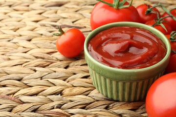 Bowl of tasty ketchup and tomatoes on wicker mat, closeup. Space for text