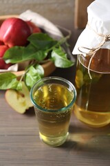 Delicious cider, red apples and green leaves on wooden table, closeup