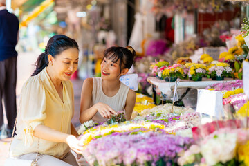 Happy Asian family mother and daughter choosing and buying colorful flowers together at florist shop street market in the city for making flowers vase arrangement on spring summer holiday vacation.