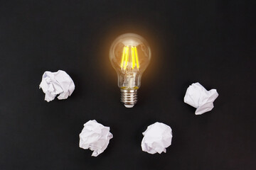 Light bulbs glows orange and crumpled paper on black background. Good idea, creativity and inspiration concept.