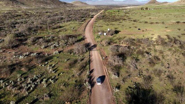 Aerial shot of car on dirt road in Willcox, Arizona, wide rotating drone shot with mountains in the background