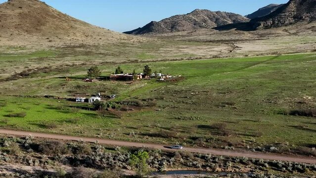 Aerial shot of car driving on dirt road in Willcox, Arizona, wide side angle drone shot with home and mountains in the background