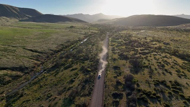 Aerial shot of car driving towards camera on dirt road in Willcox, Arizona, wide drone shot with mountains in the background and dust behind the car