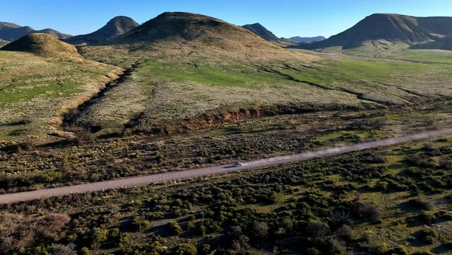 Aerial shot of car driving on dirt road in Willcox, Arizona, wide side tracking drone shot with mountains in the background and dust behind the car