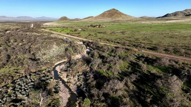 Aerial shot of car driving on dirt road in Willcox, Arizona, wide rotating side angle drone shot with mountains in the background