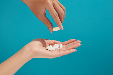 One hand is giving a white pill to another hand carrying some other pills. Concept of first aid, medical care during illness