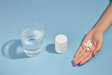A glass of water, an unlabeled medicine bottle and a handful of pills is arranged in one line on...