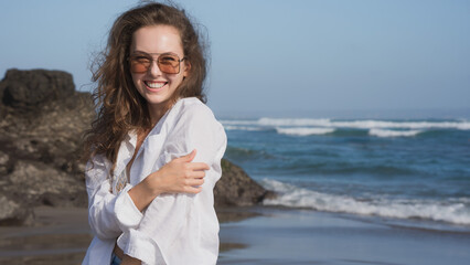 Portrait of a wealthy young woman in a white shirt and blue bikini, standing on the Bali coast of...