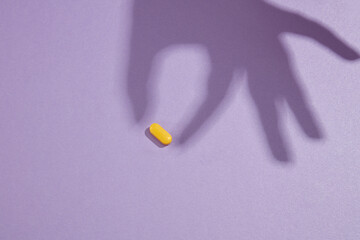 A pill isolated on the purple background with a hand shadow acting like holding the pill. Concept of medicine and health support