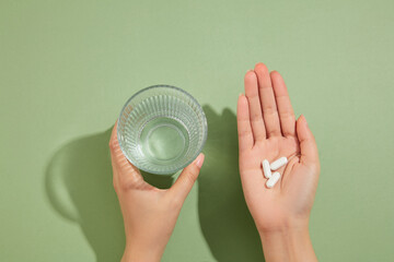 A glass of water is held in the left hand and several white pills placed on the right hand....