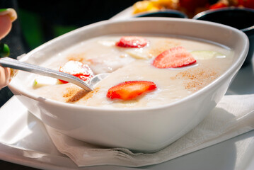 White plate served with oatmeal breakfast cereal served with strawberry slices on wooden table and sunlight.