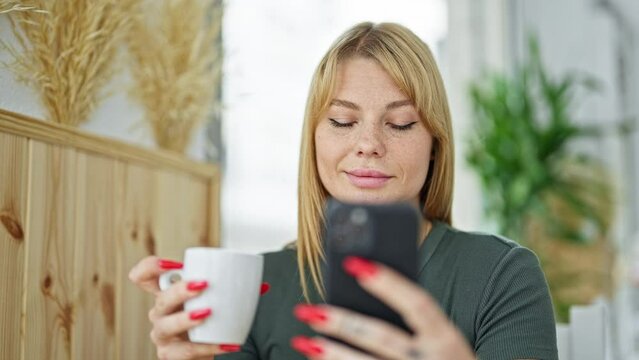 Young blonde woman using smartphone drinking coffee at coffee shop