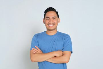Portrait of happy young Asian man in blue t-shirt standing with crossed arms, smiling at camera, looking confident isolated on white background