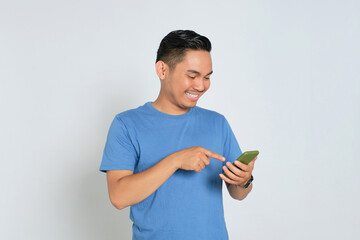 Smiling young Asian man in blue t-shirt using mobile phone, checking social media, communicating with friends isolated on white background