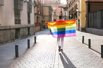 Proudly Embracing the LGBT Flag, a Backlit Man Stands with Open Arms on a Sunny City Street at...