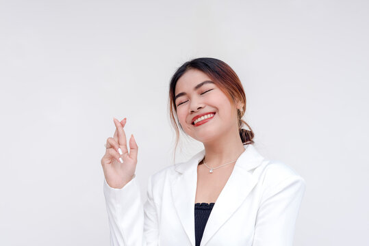 A positive and optimistic young woman holding one hand up with fingers crossed. Isolated on a white background.