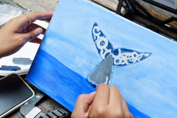 Close-up. Hands of female apprentice painter holding paintbrush. Paint  whales and sea on four...