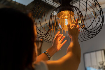 Woman changing light bulb in hanging lamp at home. Modern interior decor, house owner cleaning or...