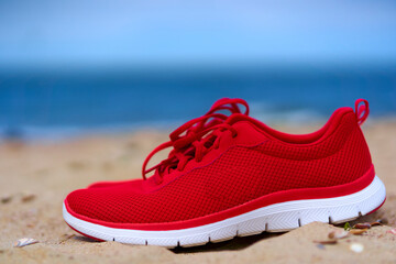 Red ladies shoes on empty sandy beach. Footwear for sport and leisure on the sea. Close up.