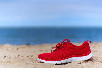 Naklejka premium Red ladies shoes on empty sandy beach. Footwear for sport and leisure on the sea. Close up.